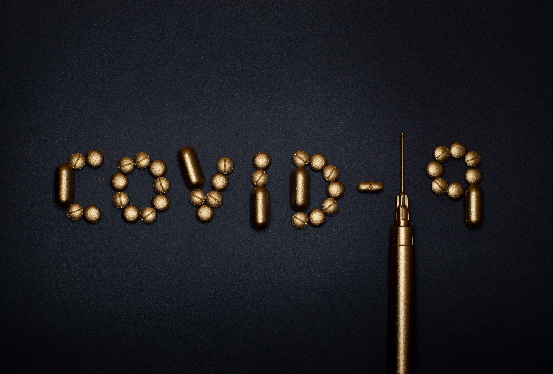 Nápis "COVID-19" vyskládaný z pilulek a z injekční stříkačky