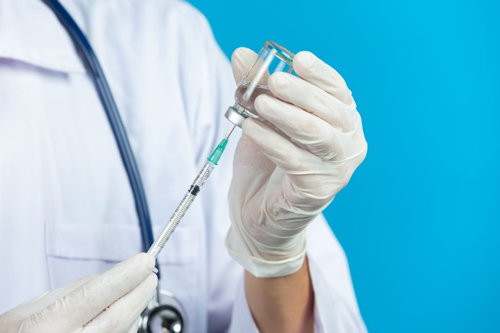 Ilustrační obrázek k téme nežádoucí účinky očkování - lékař drží v ruce stříkačku s vakcínou.