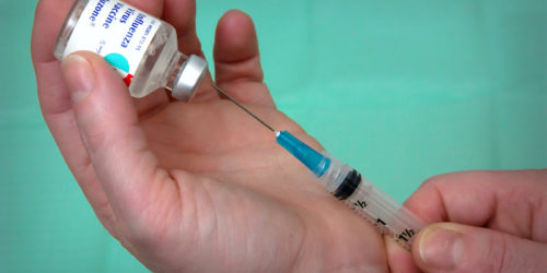 Lékař nabírá vakcínu proti chřipce do injekční stříkačky.