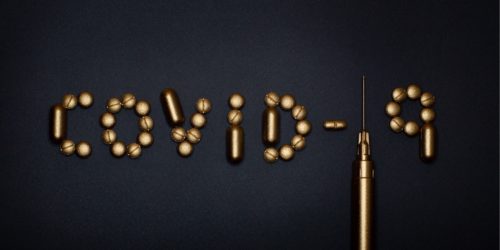 Nápis "COVID-19" vyskládaný z pilulek a z injekční stříkačky