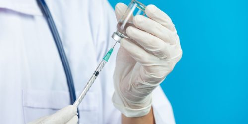 Ilustrační obrázek k téme nežádoucí účinky očkování - lékař drží v ruce stříkačku s vakcínou.